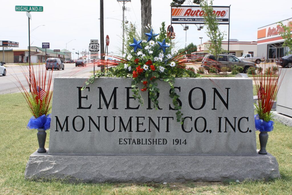 Emerson Monument Company sign with floral saddle and vases with cemetery flowers. 
